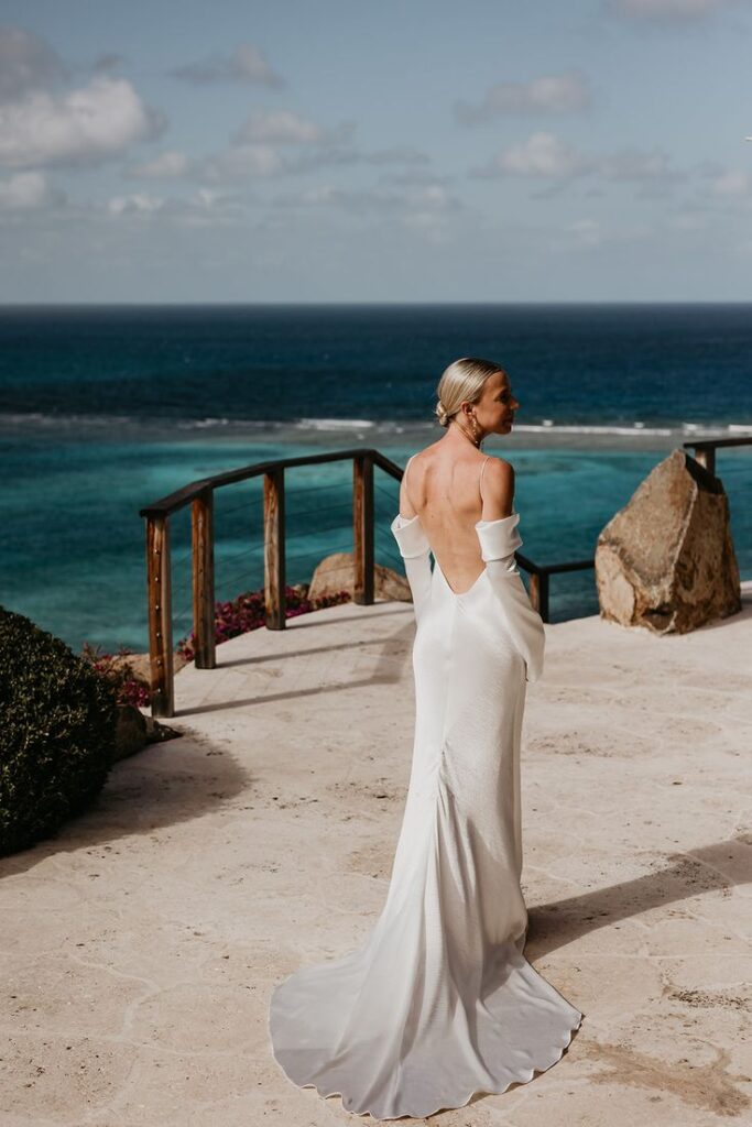 Bride is dressed in her white wedding dress looking at the blue waters of her wedding.